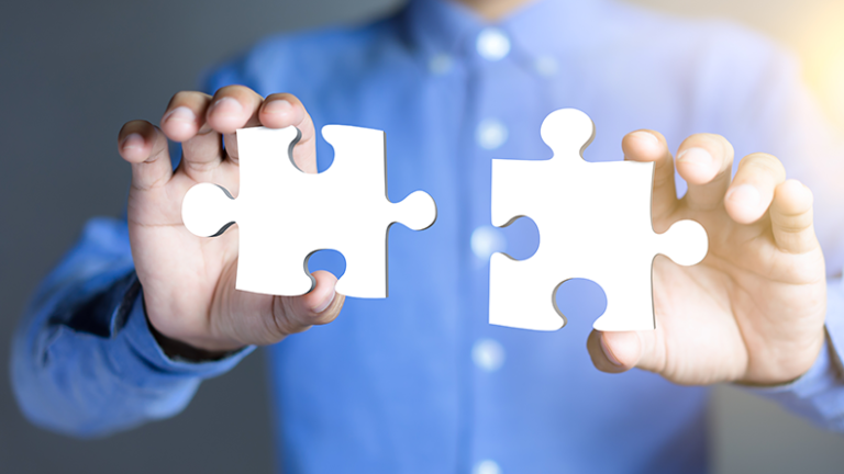 Businessman hands connecting puzzle pieces representing the merging of two companies or joint venture, partnership