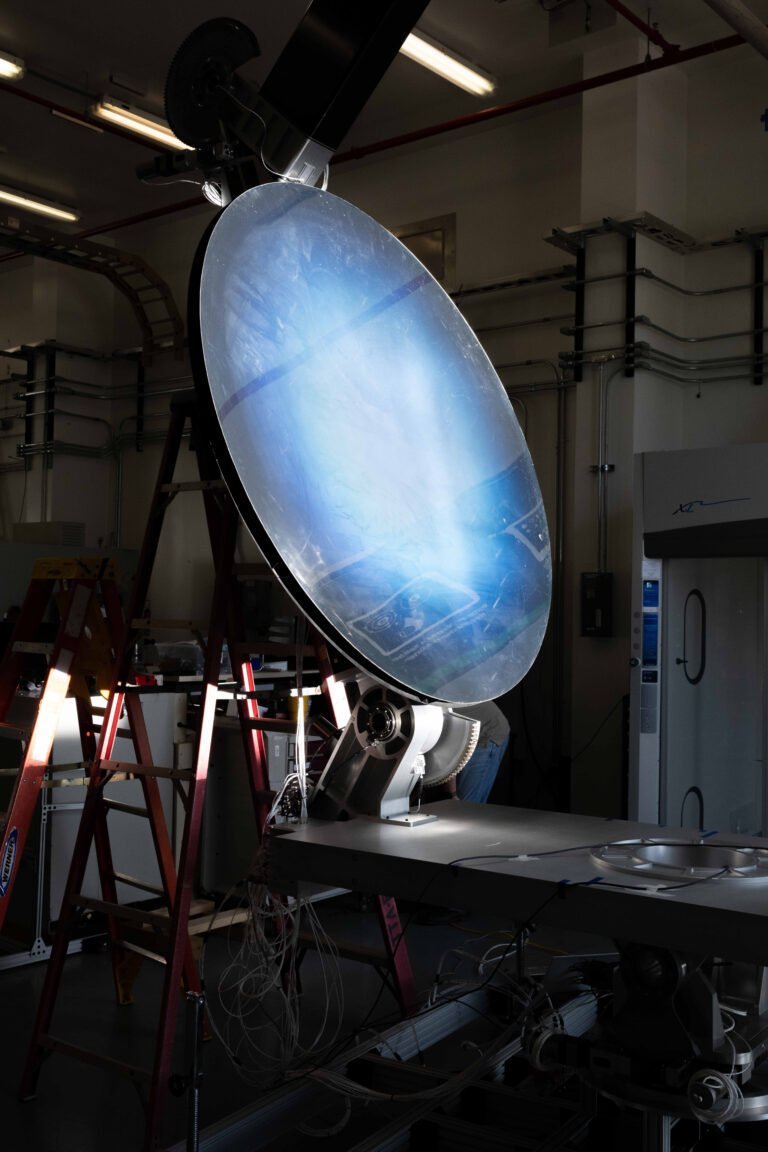 Harnessing the Sun to Extract Oxygen on the Moon Light shines onto a mirror-like solar concentrator resting on a workbench. The concentrator is tilted upward around 45 degrees to catch the light. Its surface is black at the edges, and as you move inward, it goes from a deep blue to white.