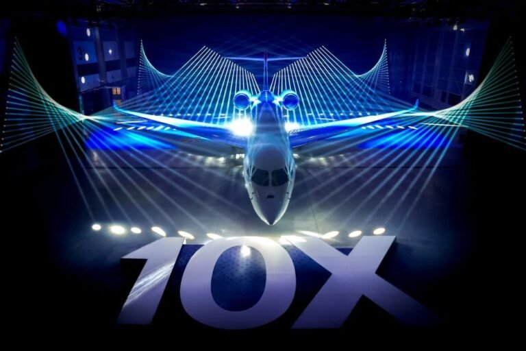 Dassault Aviation Falcon 10X viewed head-on during its rollout ceremony, dramatically lit with blue laser projections tracing the aircraft's wingspan and a large illuminated 10X sign in the foreground