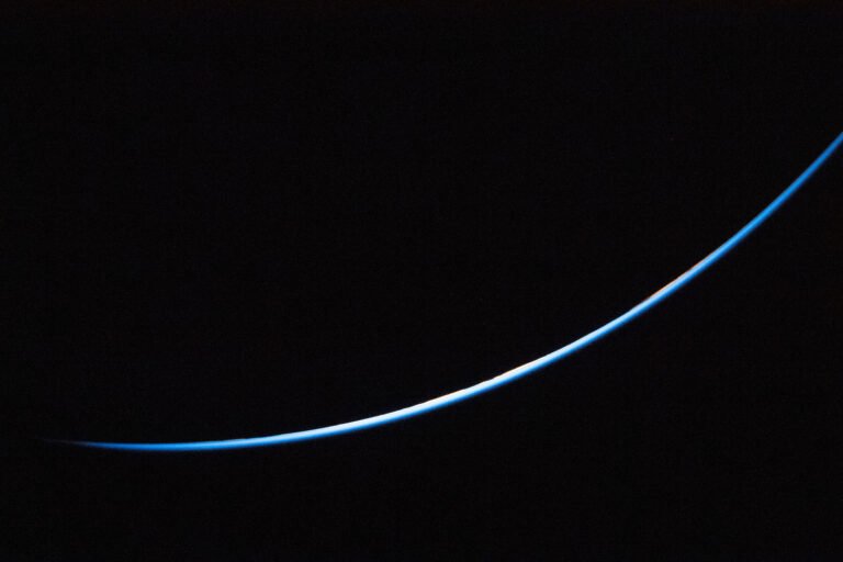 A Light in the Dark The edge of Earth is a thin line curving upward from left to right. The line is different shades of blue.
