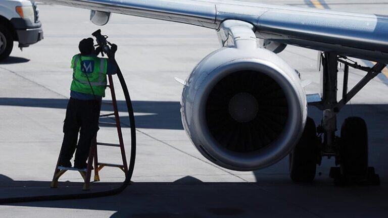 Airlines Grapple With Consequences Of Iran War’s Fuel Price Spike worker carrying refueling tube by aircraft