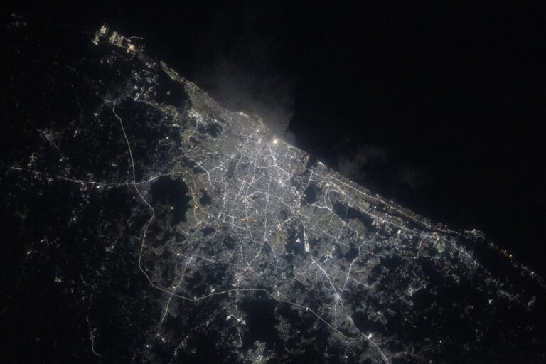 A view of Chennai at night from the International Space Station shows a sprawling city along the water (upper right). City lights make the city shine while also highlighting roadways. The surrounding area is mostly dark.