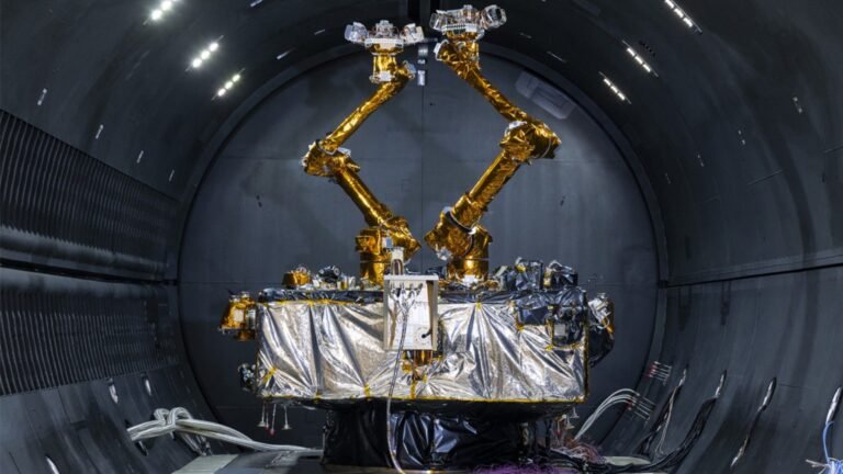 a cube-shaped satellite with two multi-jointed arms inside a cleanroom