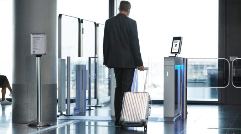 A male pasenger in a dark suit pulls a small suitcase through passenger check-in.