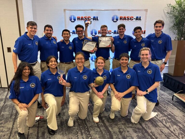 NASA Announces Winners of 2026 University Innovation Competition A group of 14 students wearing blue polo shirts smile at the camera while holding the first place certificate for winning the NASA RASC-AL challenge.