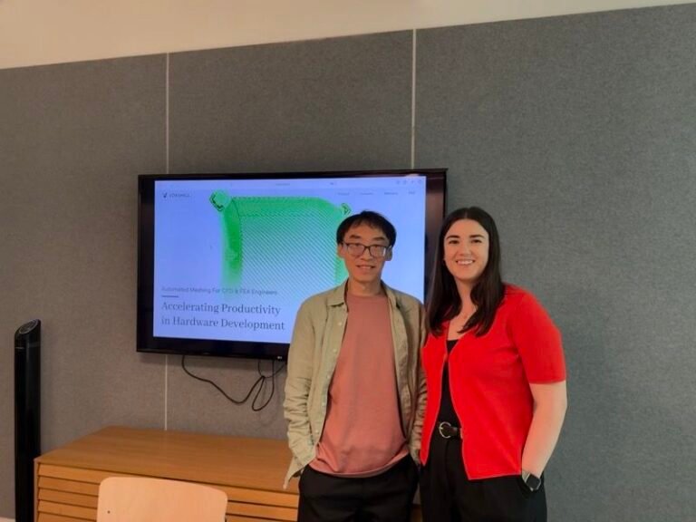 Two people standing in front of a screen displaying the Voxshell website and a mesh model of an engineering component