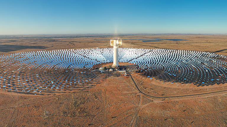 Expansive array of mirrors surround Khi Solar One concentrated solar tower in dry desert landscape of South Africa.