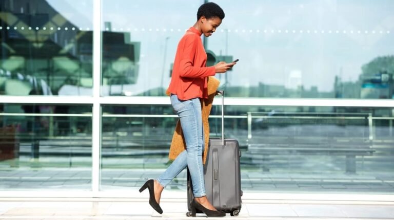 Mishandled bag rates fell by 23% in 2025, yet still cost industry US$6.3bn A woman wearing a red jacket and light blue trousers walks through an airport pulling a small piece of luggage.