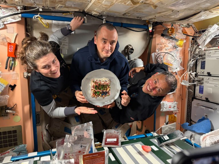 From left, Expedition 74 flight engineers Anna Kikina and Pyotr Dubrov of Roscosmos, and Anil Menon of NASA pose for a portrait while holding a cake celebrating their recent arrival aboard the International Space Station.