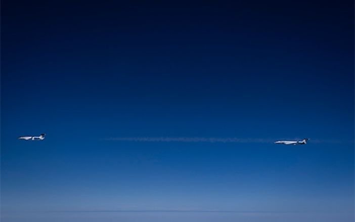 Rolls-Royce studies contrail impact of SAF at high altitudes Two business jets flying in close formation at high altitude, with a thin contrail trailing between them against a deep blue sky