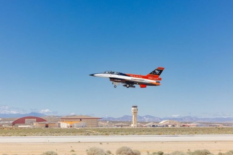 The orange, white and blue X-62 VISTA, a modified F-16, takes off from Edwards Air Force Base with the control tower behind