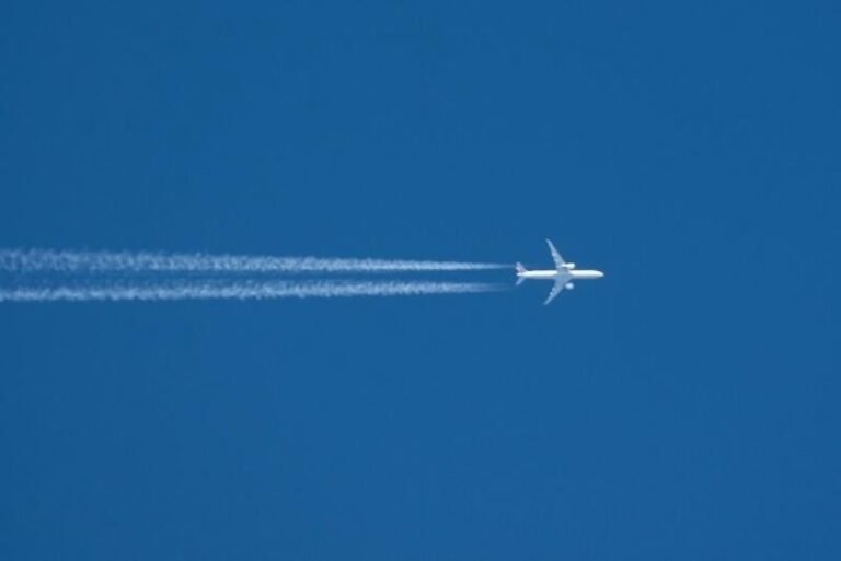 passenger aircraft flies across blue sky leaving contrails behind