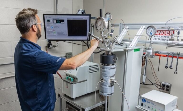 Greene Tweed adds cryogenic and supercritical CO₂ testing capabilites A technician wearing safety glasses adjusts fittings on a supercritical carbon dioxide test rig, alongside a data monitor, pressure gauges and an insulated pressure vessel in a laboratory