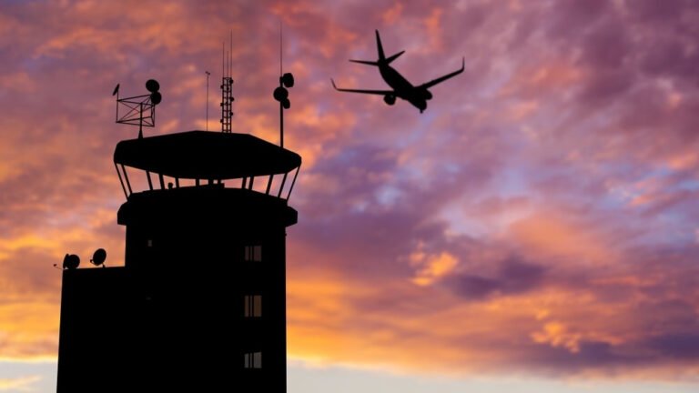 Silhouette of air traffic control (ATC) tower during sunset with airplane flying overhead