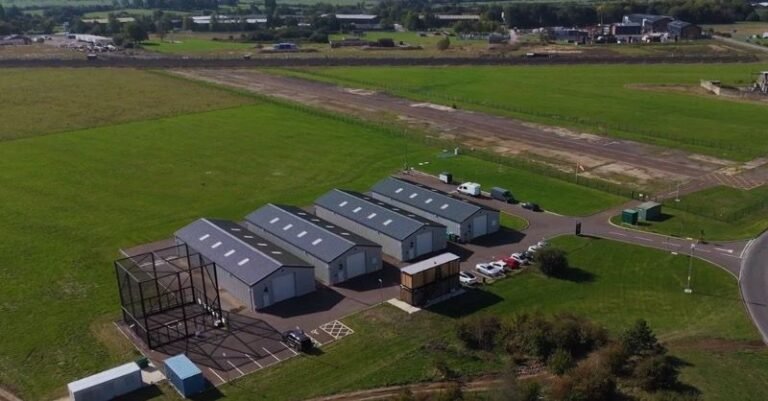 UK expands national drone testing center with new capabilities Aerial view of the drone testing facility at Westcott Venture Park, with hangars, a control building, parking and a test area beside a runway in open countryside